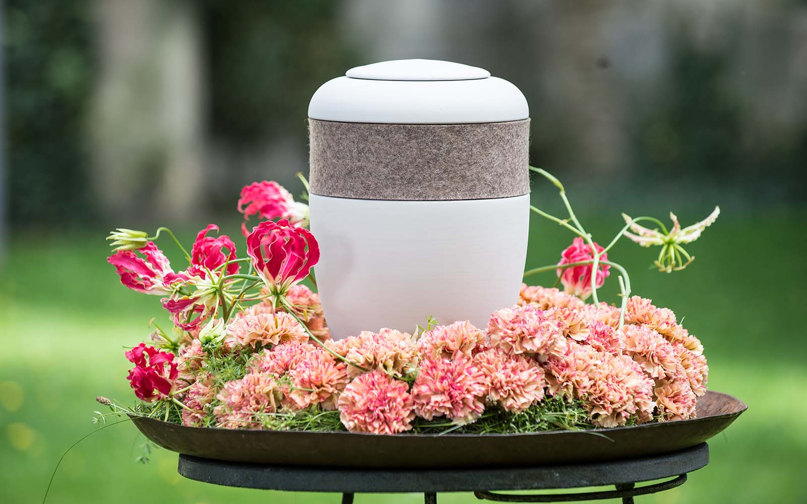 Cremeweiße Bio-Urne mit Kaschmir-Filzring, in Metallschale mit Blumenkranz, präsentiert schlichte Eleganz und Qualität